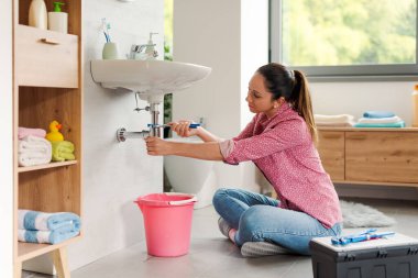 Becerikli genç kadın banyo lavabosunu kendi başına tamir ediyor. Su pompası kullanıyor.