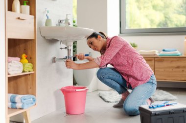Becerikli genç kadın banyo lavabosunu kendi başına tamir ediyor. Su pompası kullanıyor.