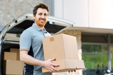 Paket taşıyan ve sokakta yürüyen gülümseyen bir teslimatçının portresi.