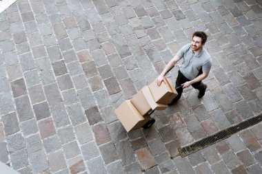 Teslimatçı bir el arabasını sokağa itiyor ve müşterilere paket teslim ediyor.