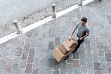 Teslimatçı bir el arabasını sokağa itiyor ve müşterilere paket teslim ediyor.