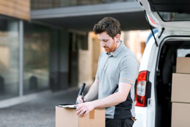 Profesyonel kurye teslimat belgelerini kontrol ediyor ve paketleri teslim ediyor.
