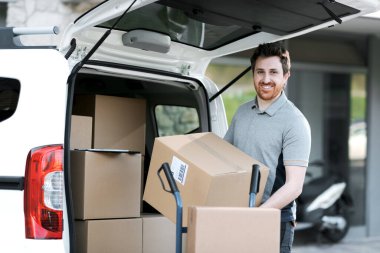 Teslimatçı bir minivanın içinde kutuları alıyor ve bir el arabası yüklüyor, hızlı teslimat ve taşınma konsepti