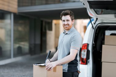 İşteki kendine güvenen teslimatçı teslimat belgelerini kontrol ediyor ve gülümsüyor.