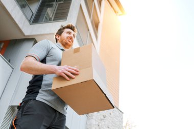 Profesyonel gülen teslimatçı. Elinde kutular, sokakta yürüyor.