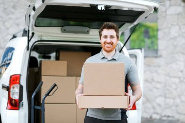 Kutuları taşıyan gülümseyen profesyonel teslimatçı, paketleri bir minivana yüklüyor.