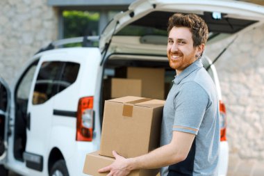 Kutuları taşıyan gülümseyen profesyonel teslimatçı, paketleri bir minivana yüklüyor.