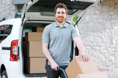 Çalışan müşterilere paket teslimatı yapıyor, bir el arabası kullanıyor ve şehir caddesinde kutu taşıyor.