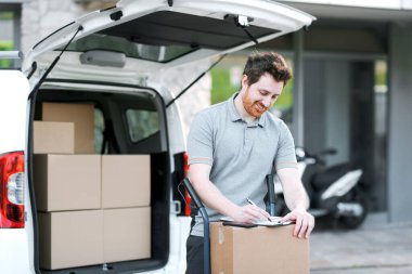 İşteki kendine güvenen teslimatçı teslimat belgelerini kontrol ediyor ve gülümsüyor.