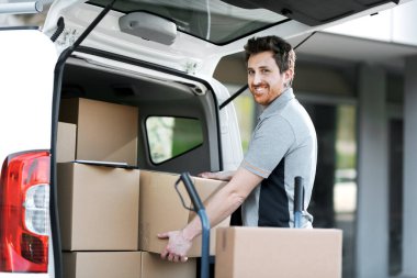 Teslimatçı bir minivanın içinde kutuları alıyor ve bir el arabası yüklüyor, hızlı teslimat ve taşınma konsepti