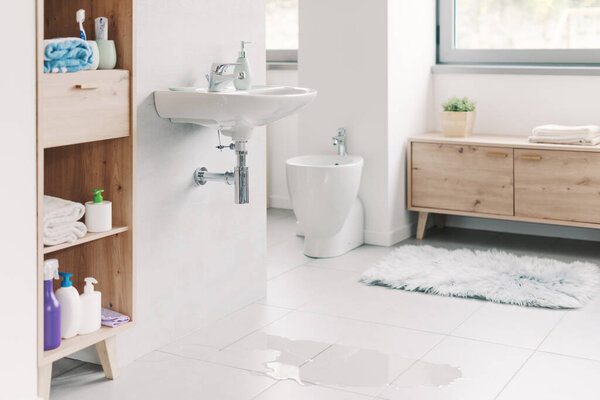 Leaking sink in the bathroom and puddle of water on the floor