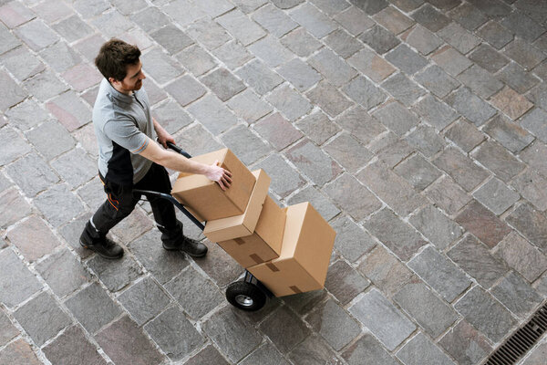 Доставщик толкает ручной грузовик по улице и доставляет посылки клиентам