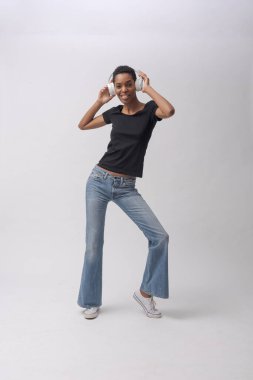 Güzel fit siyah kadın kulaklık takıyor ve dans ediyor, müzik ve kulüp konsepti, tam boy, beyaz arka planda izole edilmiş.