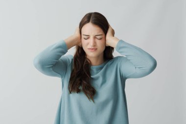 Stresli, yorgun bir kadın elleriyle kulaklarını kapatıyor. Sinirli ve üzgün.