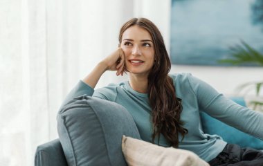 Güzel bir genç kadının portresi kanepede oturuyor ve evde dinleniyor, başka yere bakıyor ve gülümsüyor.