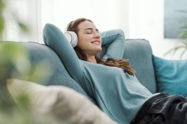 Mutlu kadın evdeki kanepede dinleniyor ve kulaklıkla müzik dinliyor.
