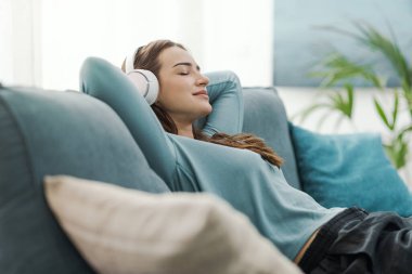 Mutlu kadın evdeki kanepede dinleniyor ve kulaklıkla müzik dinliyor.
