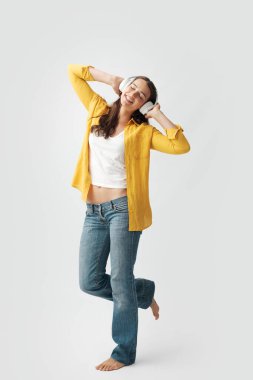 Mutlu moda kadın ayakta ve çıplak ayakla dans ediyor, kablosuz kulaklık, müzik ve eğlence konsepti takıyor.