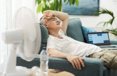 Yorgun adam kanepede oturup sıcaktan, yaz sıcağı kavramından muzdarip.