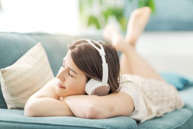 Güzel, sakin bir kadın kanepede uzanıyor ve kulaklık takıyor. Gözleri kapalı müzik dinliyor.