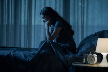 Çaresiz genç bir kadın geceleri yatakta yalnız oturuyor, depresyonda ve uykusuzluk çekiyor.