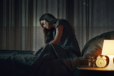 Çaresiz genç bir kadın geceleri yatakta yalnız oturuyor, depresyonda ve uykusuzluk çekiyor.