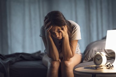 Depresyondaki kadın geceleri yatakta oturuyor, üzgün ve uykusuzluk çekiyor.