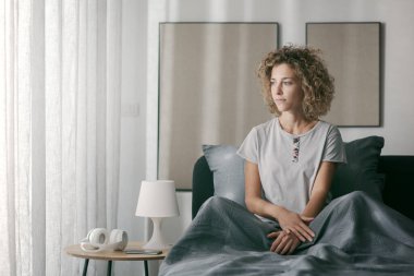 Rahatlamış kadın yatağında oturuyor ve başka tarafa bakıyor, uyanıyor.