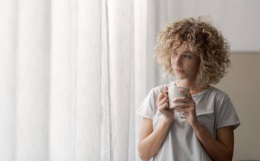 Pencereden dışarı bakıp kahve içen uykulu kadın uyandı.