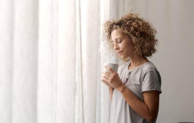 Rahatlamış kadın kahvaltı yapıyor ve pencereden dışarı bakıyor, dingin ve kahve içiyor.