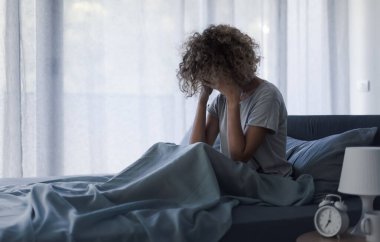 Mutsuz bir kadın uyanıyor ve elleri yatağında oturuyor.