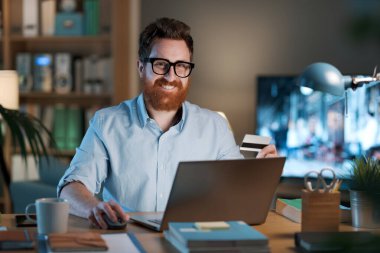 Ev ofisinde çalışan kendine güvenen bir işadamı, çevrimiçi alışveriş ve çevrimiçi bankacılık kavramı olan bir kredi kartı kullanıyor.