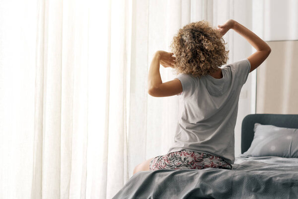 Кудрявая женщина просыпается и вытягивает руки, вид сзади, копирует пространство