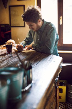 Genç hipster adam rustik ahşap bir masa üstünde bir defter üzerinde onun öğle yemeği molası sırasında çizimi