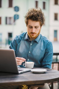 Genç hippi barda kahve molası veriyor ve dizüstü bilgisayar kullanıyor.