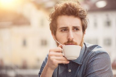 Hipster adam bir kapuçino barda, o uzakta dalgın ve seyir.