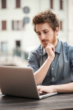 Arka plan üzerinde şehir ile açık bir tablo üzerinde bir dizüstü bilgisayar üzerinde çalışan genç hipster adam