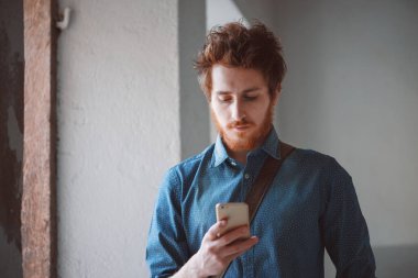 Hippi genç adam yürüyor ve cep telefonuyla mesajlaşıyor.