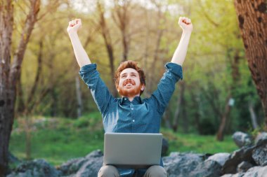 Mutlu neşeli hipster adam açık havada doğa, özgürlük ve mutluluk kavramı içinde oturan bir dizüstü bilgisayar ile