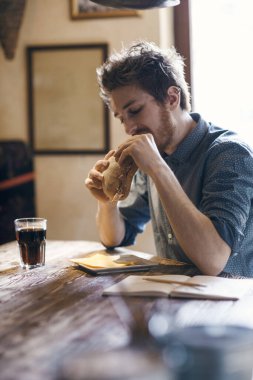 Aç genç hippi, mutfak masasında oturmuş jambonlu lezzetli bir sandviç yiyor.