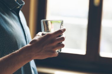 Pencerenin yanında bir bardak tutan genç bir erkek.