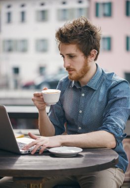 Bardaki bir dizüstü bilgisayar ile bağlantı ve şehir binaları arka plan üzerinde bir kapuçino, içme genç adam