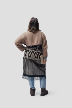 Tarz sahibi bir kadın elinde bir defter, arkasına bakıyor, uzun boylu, beyaz arka planda soyutlanmış.