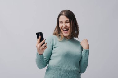 Mutlu kazanan kadın akıllı telefon ekranına bakıyor ve zaferini kutluyor, beyaz arka planda izole edilmiş.