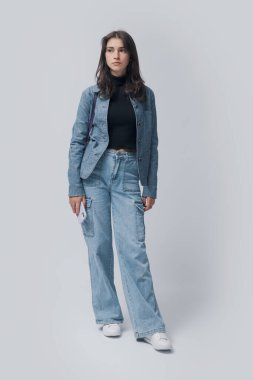 Genç ve güzel bir kadının uzun bir portresi ayakta dikiliyor ve diğer tarafa bakıyor. Akıllı telefonunu beyaz arka planda tek başına tutuyor.