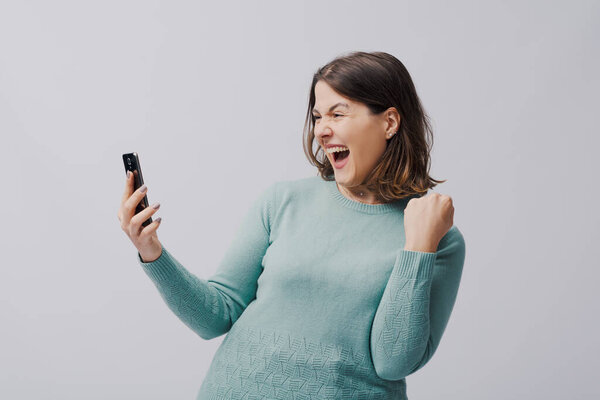Happy winner woman looking at her smartphone screen and celebrating her victory, isolated on white background
