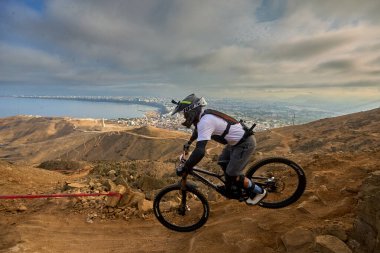 Yokuş aşağı bir MTB binicisi, arka planda Pasifik Okyanusu ve Lima şehrinin görkemli manzarasıyla El Morro Solar 'ın engebeli hatlarını oyuyor..