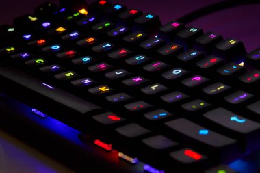 Renkli bir RGB mekanik oyun klavyesinin yakın çekimi canlı renklerle aydınlatılmış. Oyun ayarları için tasarlanmış modern bilgisayar aksesuarı, kişiselleştirilebilir arka ışıklandırma ve şık tasarım. 