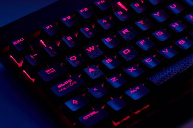 Renkli bir RGB mekanik oyun klavyesinin yakın çekimi canlı renklerle aydınlatılmış. Oyun ayarları için tasarlanmış modern bilgisayar aksesuarı, kişiselleştirilebilir arka ışıklandırma ve şık tasarım. 