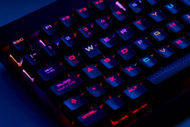 Renkli bir RGB mekanik oyun klavyesinin yakın çekimi canlı renklerle aydınlatılmış. Oyun ayarları için tasarlanmış modern bilgisayar aksesuarı, kişiselleştirilebilir arka ışıklandırma ve şık tasarım. 